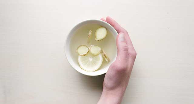 Hand holding teacup containing Organic Apple Cider Vinegar with lemon and ginger.