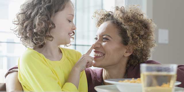 Young girl touching her mother on the nose as she has breakfast.