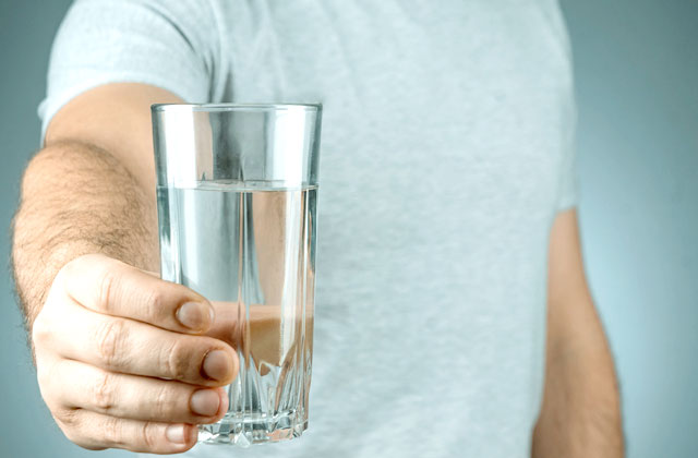 Man holding glass of water. Taking selenium in liquid form increases bioavailability, enabling effective absorption of the mineral.