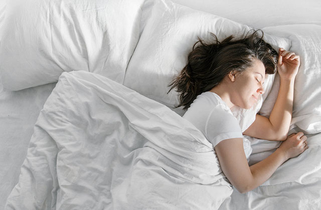 Woman sleeping in a bed. Magnesium can assist with alleviating muscle cramps at night.