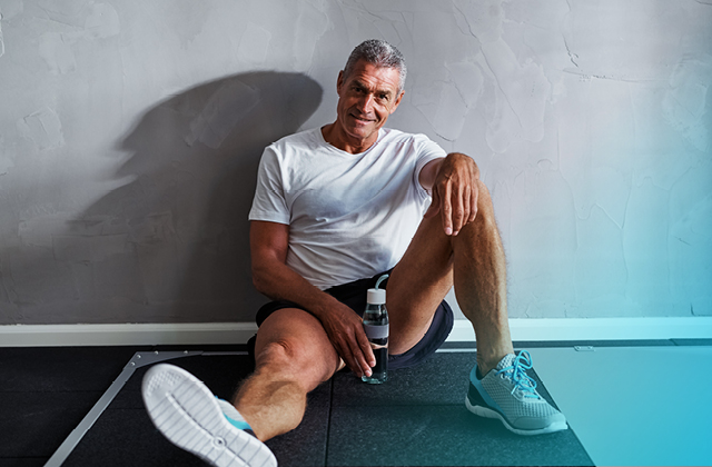 Man sitting against gym wall with water bottle after exercise.