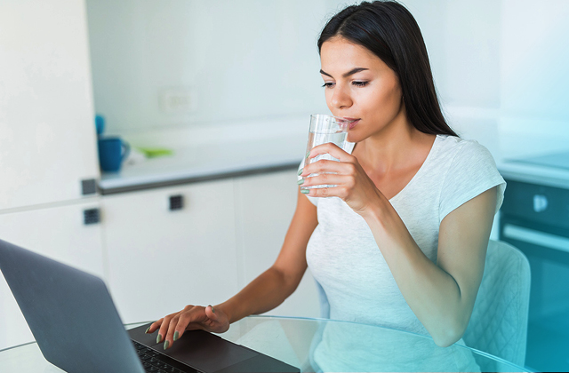 Women drinking liquid mineral supplement while working on computer.