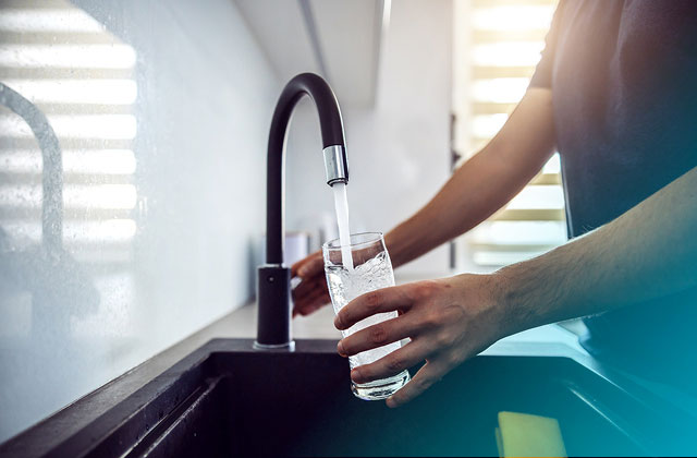 Man filling glass of water from kitchen tap